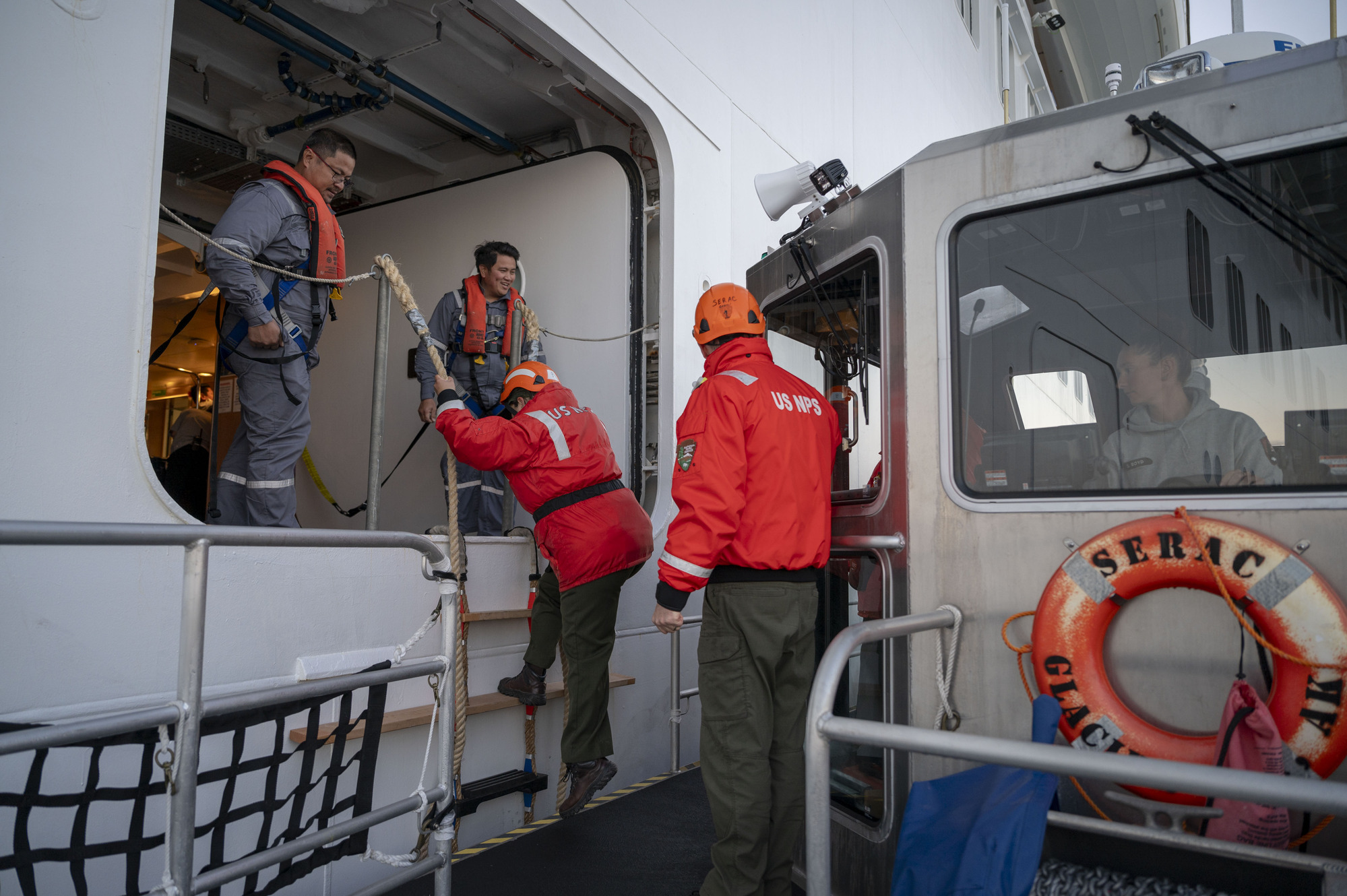 A person climbs a ladder into an opening on a cruise ship as a boat captain looks on while driving.