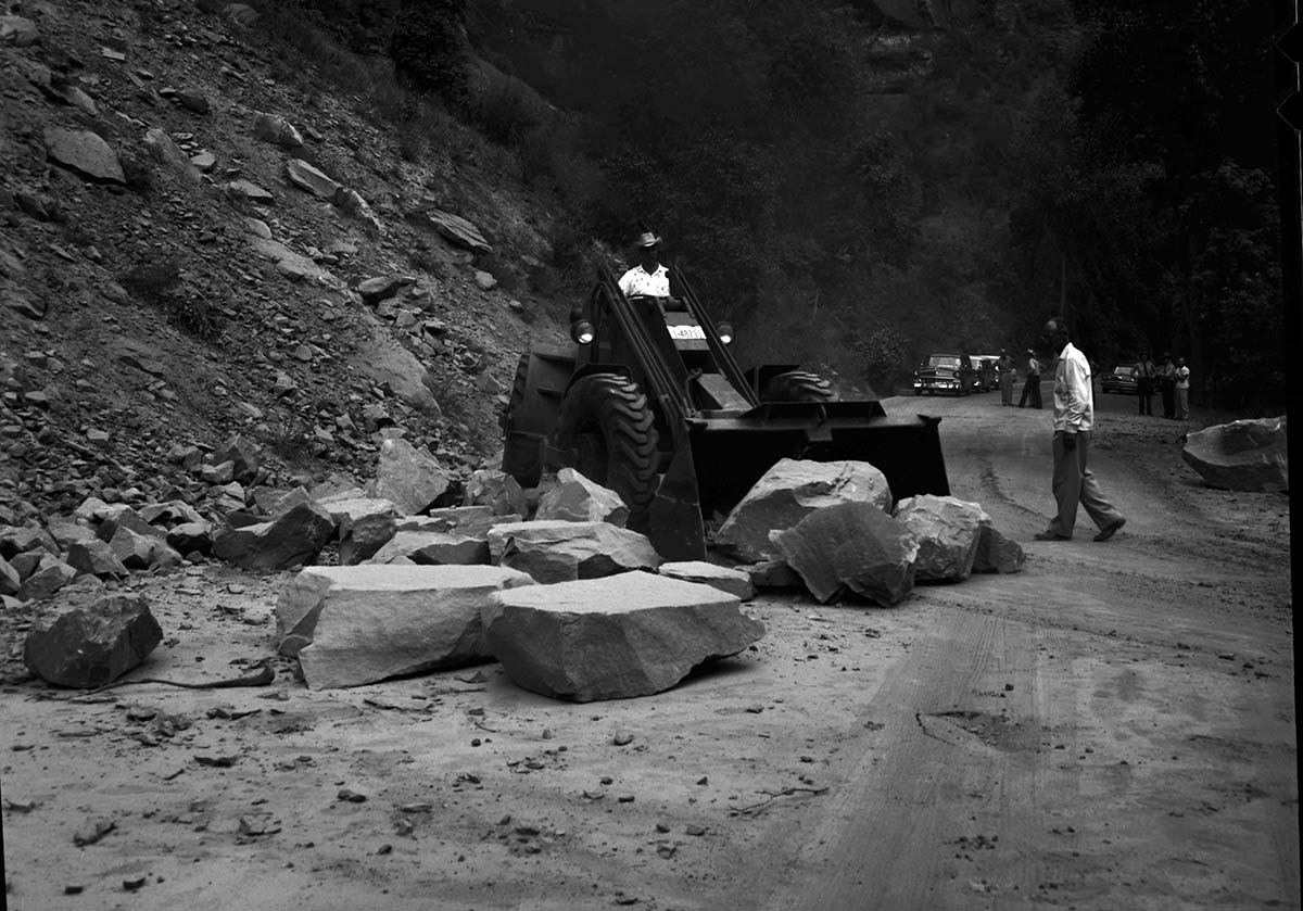 B&W negative of rock slide. Removing rocks from road with tractor- bystanders watching. [scratches, pits]