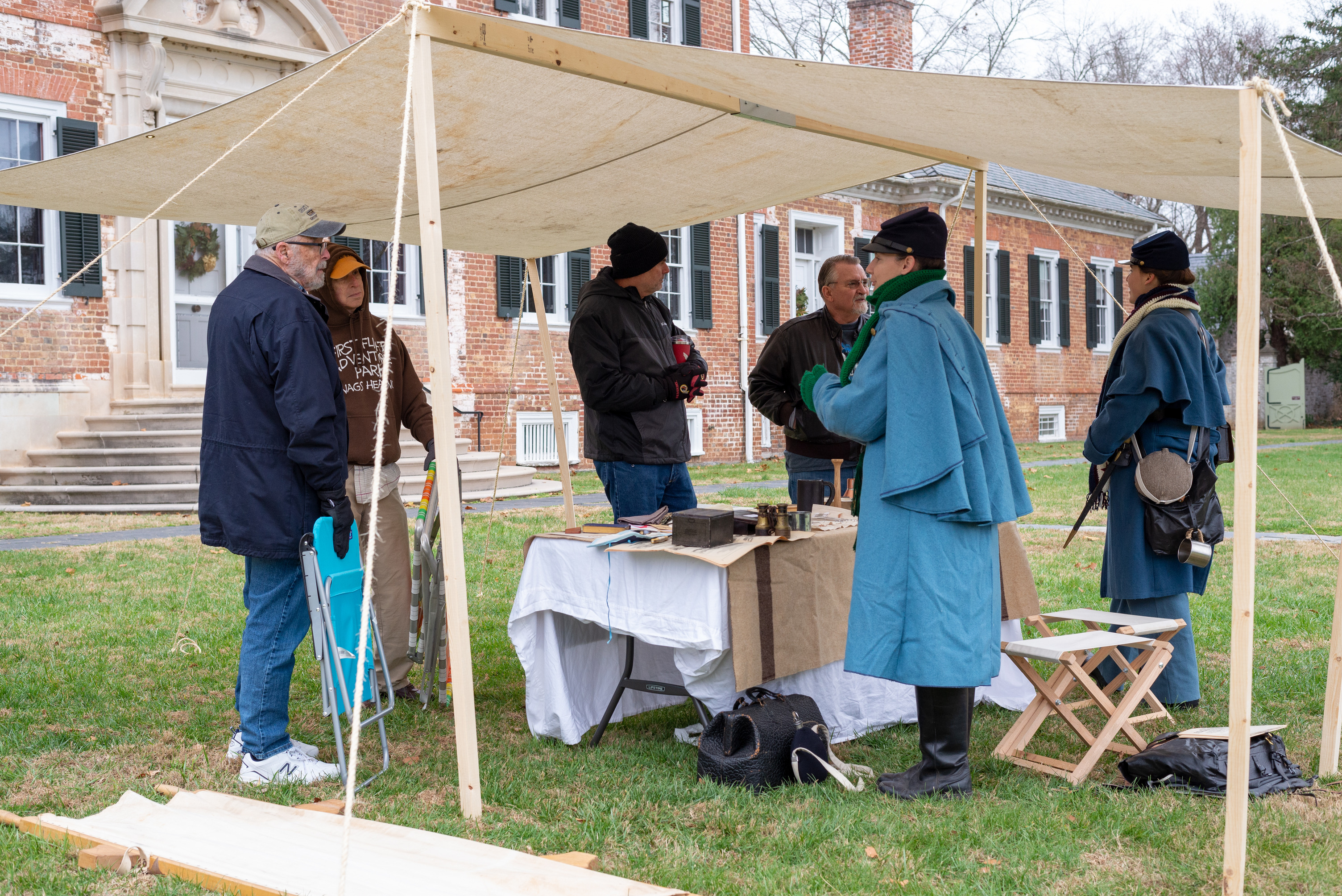Two living historians dressed as a Union doctor and soldier stands at a table with medical supplies speaking to three men.