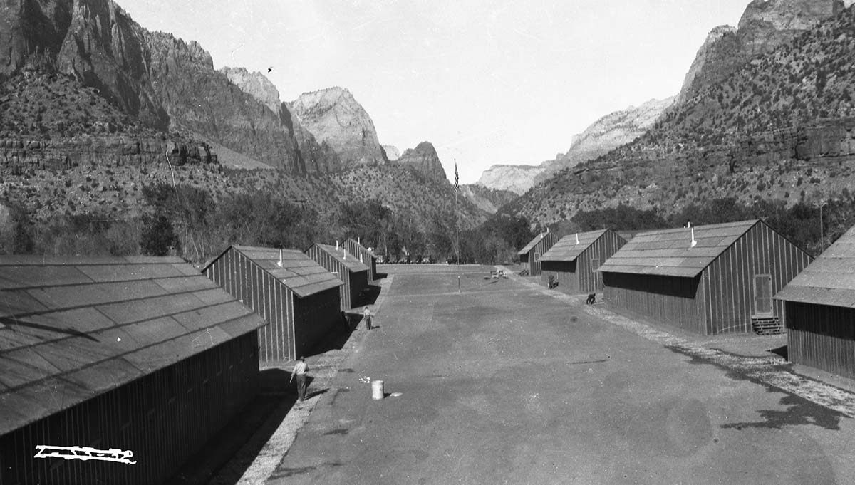 Civilian Conservation Corps (CCC) Camp NP-4, east of Virgin River, with two rows of metal building (housing?) And a Civilian Conservation Corps (CCC) worker in left foreground.