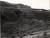 Black and white photograph of a canyon. Buildings can be seen on the hill above.