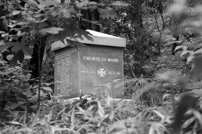 Black and white modern-day photograph of a Civil War Monument of a squat rectangle with the text "Twentieth Maine" and a cross.