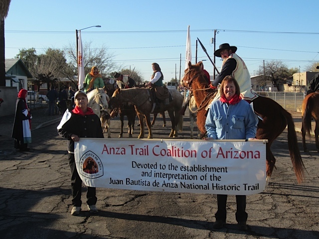 Two people wearing red bandanas around their neck hold an Anza Trail Coalition of Arizona banner in a parade