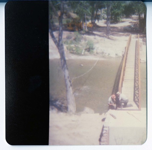 Two men working on the new Grotto footbridge across the Virgin River, equipment in background. Before trail created to access bridge.