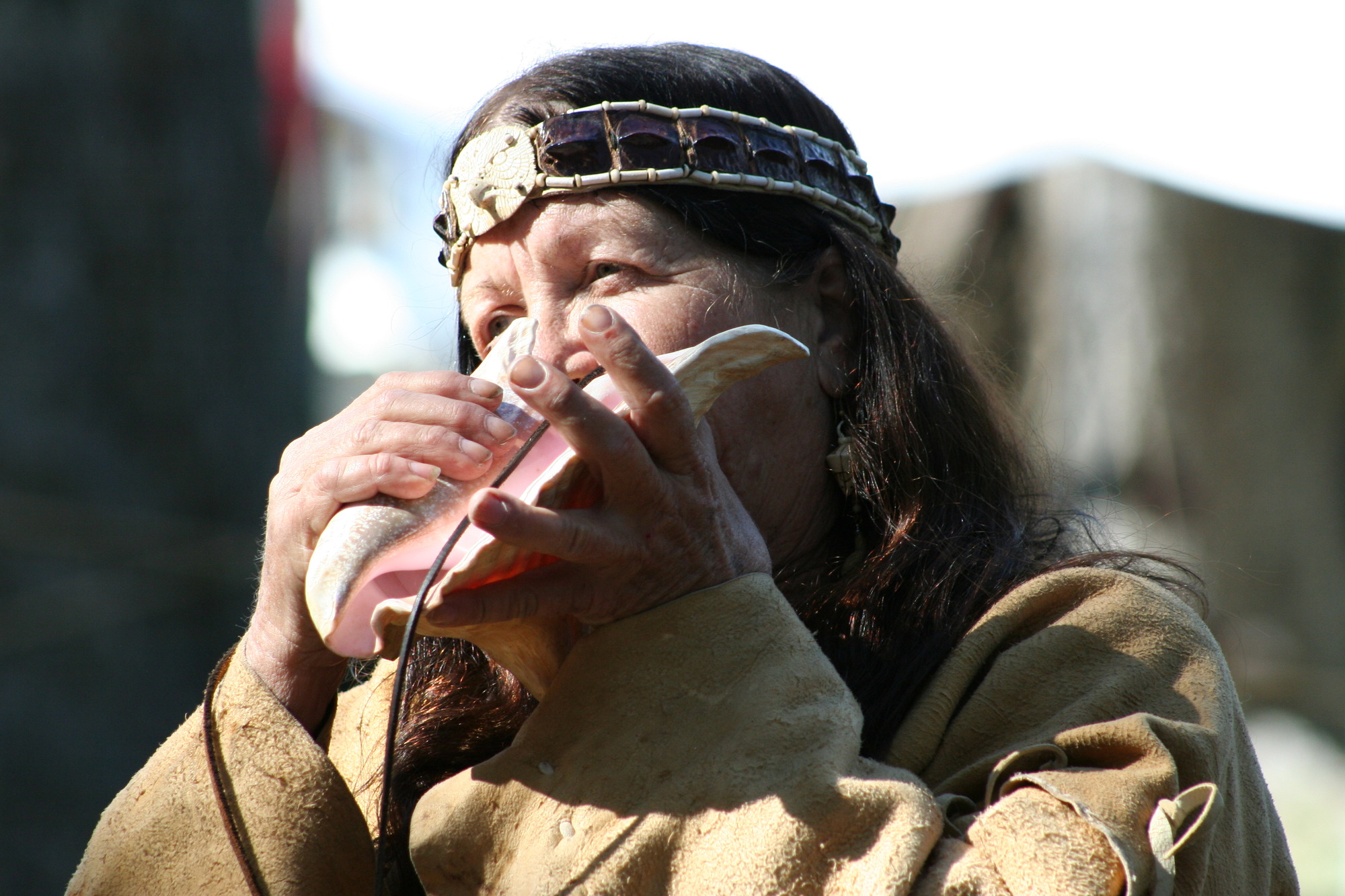 woman in leather blows on conch shell 