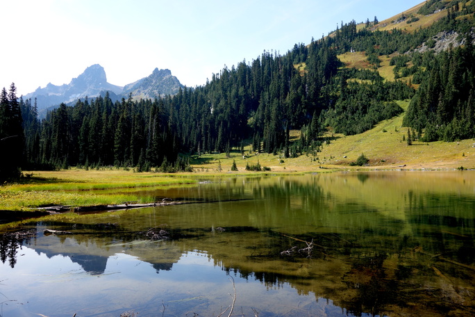 A still mountain lake reflects a forested ridge  and a rocky peak. 