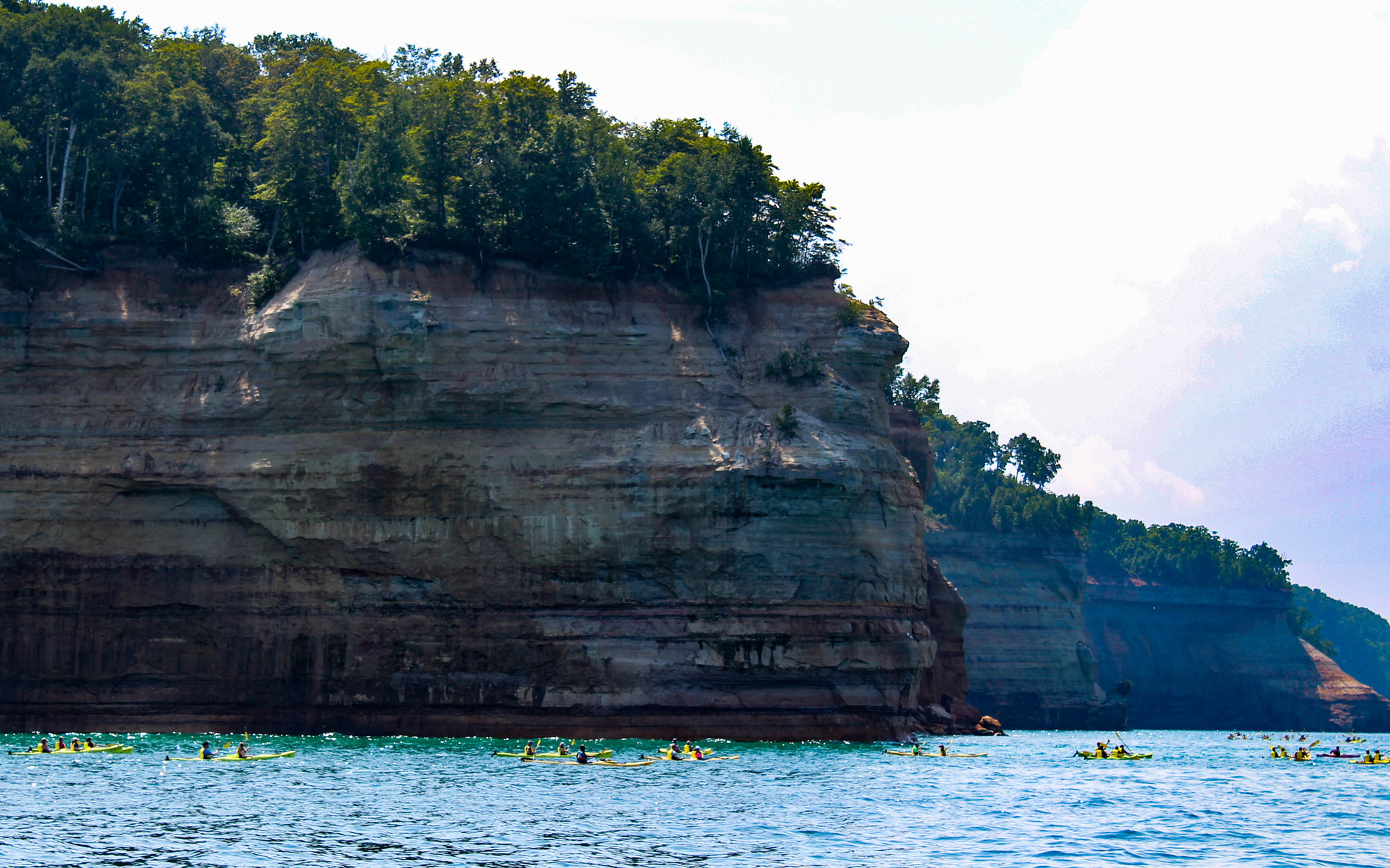 Kayakers near a long cliff face in a lake
