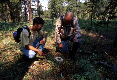 Two men kneeling looking down at a bench mark