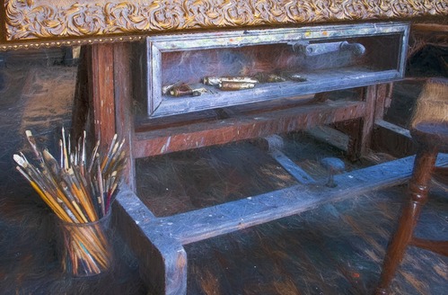 An image of an easel with several brushes in a cup next to it.