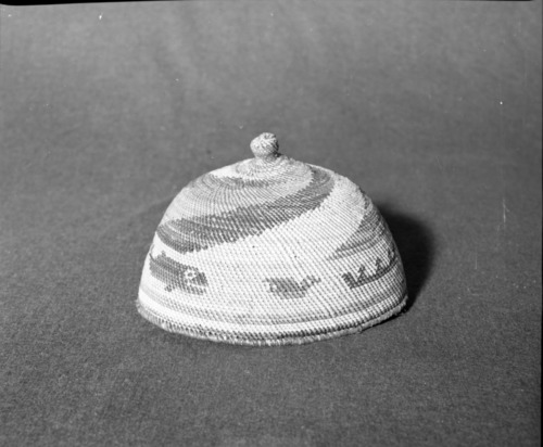 Marie Rozier Collection, Catalog No. 80. Object: Makah hat. Dimensions: 5 x 7 1/2". Materials: Red cedar, grass, raffia, dyes. Collection History: Bought from Matilda McCarty's husband off bedroom wall of their home in Washington in 1949 for $5. Made during wartime for ceremony in Seattle. Weaver said dyes were no good.  Photographed by Michael Dixon in December 1982. Catalogued by Craig Bates and Barbara Beroza. Yosemite Collections, National Park Service.