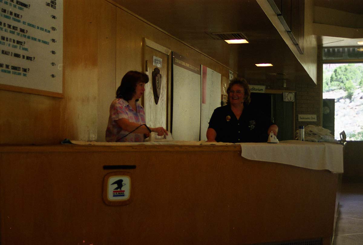 Color Photos of administration personnel. Two women at Mission 66 Visitor Center and Museum desk ironing cloths.