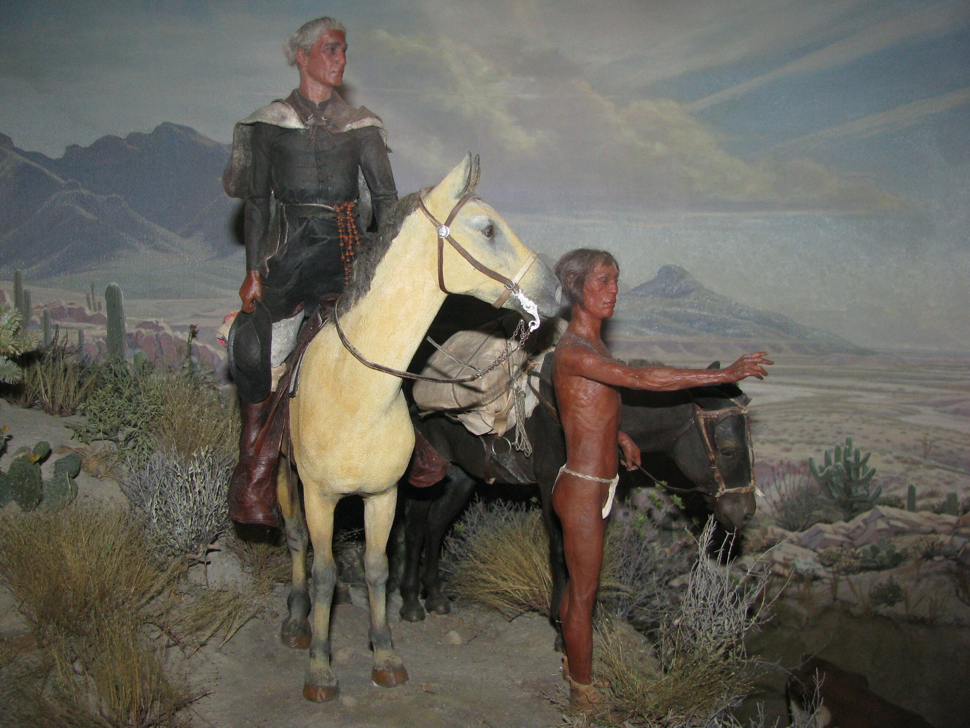 diorama depicting black-robed priest on horseback with O'odham guide in front of desert landscape