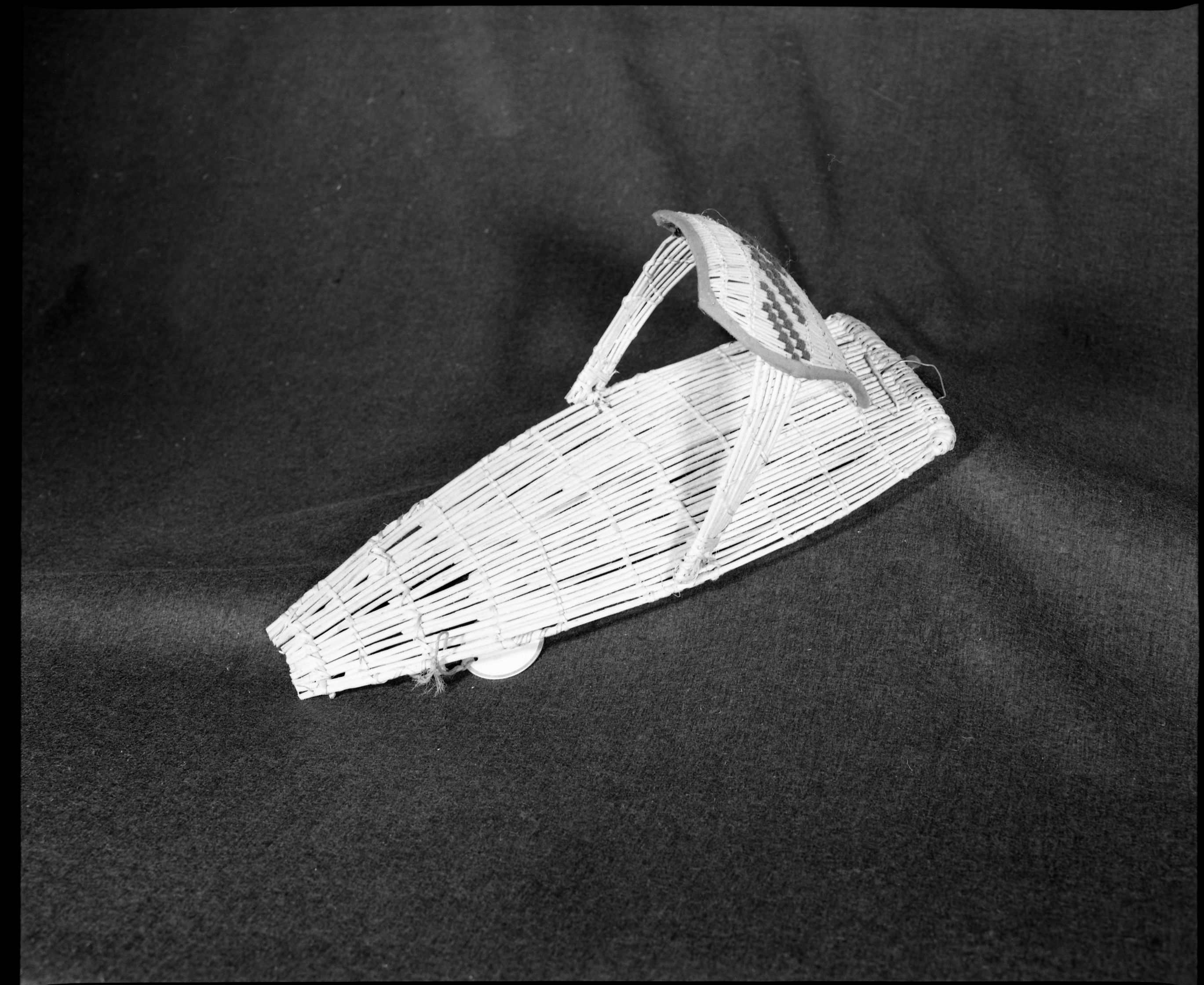 Marie Rozier Collection, Catalog No. 56. Object: Model Washoe cradlebasket. Dimensions: 16 x 6 1/2". Materials: Willow, yarn, cotton cloth. Technology: Plain twined backboard, diagonally twined hood, up to right slant of turns. Collection HIstory: Purchased by Mary Long, ca. 1950. Photographed by Michael Dixon, December 1982. Catalogued by Craig Bates and Barbara Beroza. Yosemite Collections, National Park Service.
