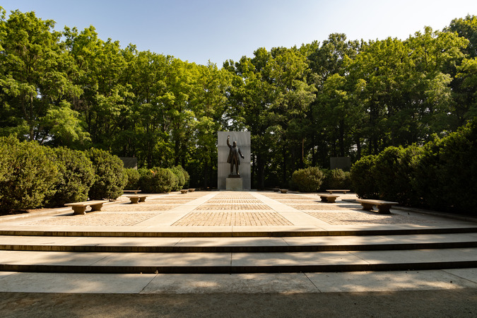 A large statue of Theodore Roosevelt at the end of a plaza surrounded by trees. 