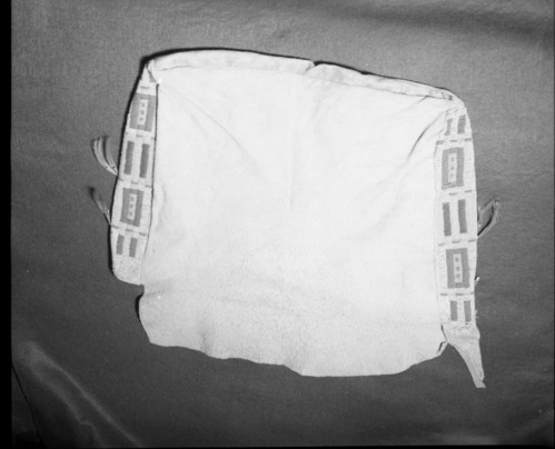 Mrs. Geraldine McConnell Collection. Object: Plains type beaded bag. Dimensions: Front - 22" x 13 1/2" Back - 18 1/2" x 18" wide at top and 16" wide at bottom. Side panels - 2 1/2" x 13 1/2" Bottom panel - 1 1/4" x 16 1/2". Technology & Materials: Brain tanned hide, sinew sewn with overcast stitch, turned right side out when completed. No welts used in seams. Beaded in lazy stitch in sinew using italian beads in opaque pink, dark blue, greasy yellow, turquoise, transparent clear, dark green, and medium blue. Three ties on body of sack with no matching holes on flap. In center top of front panel a 2" slit was made in the hide and sewn up with sinew, perhaps to take in excess hide. Brain tanned hide tabs project 5" from each side panel. Analine dyed horsehair emitting from tin cones completes decoration. Collection History: Purchased in a store in Mariposa, c. 1930's. Photographed by Michael Dixon January 1983. Catalogued by Craig Bates and Barbara Beroza. Yosemite collections, National Park Service.