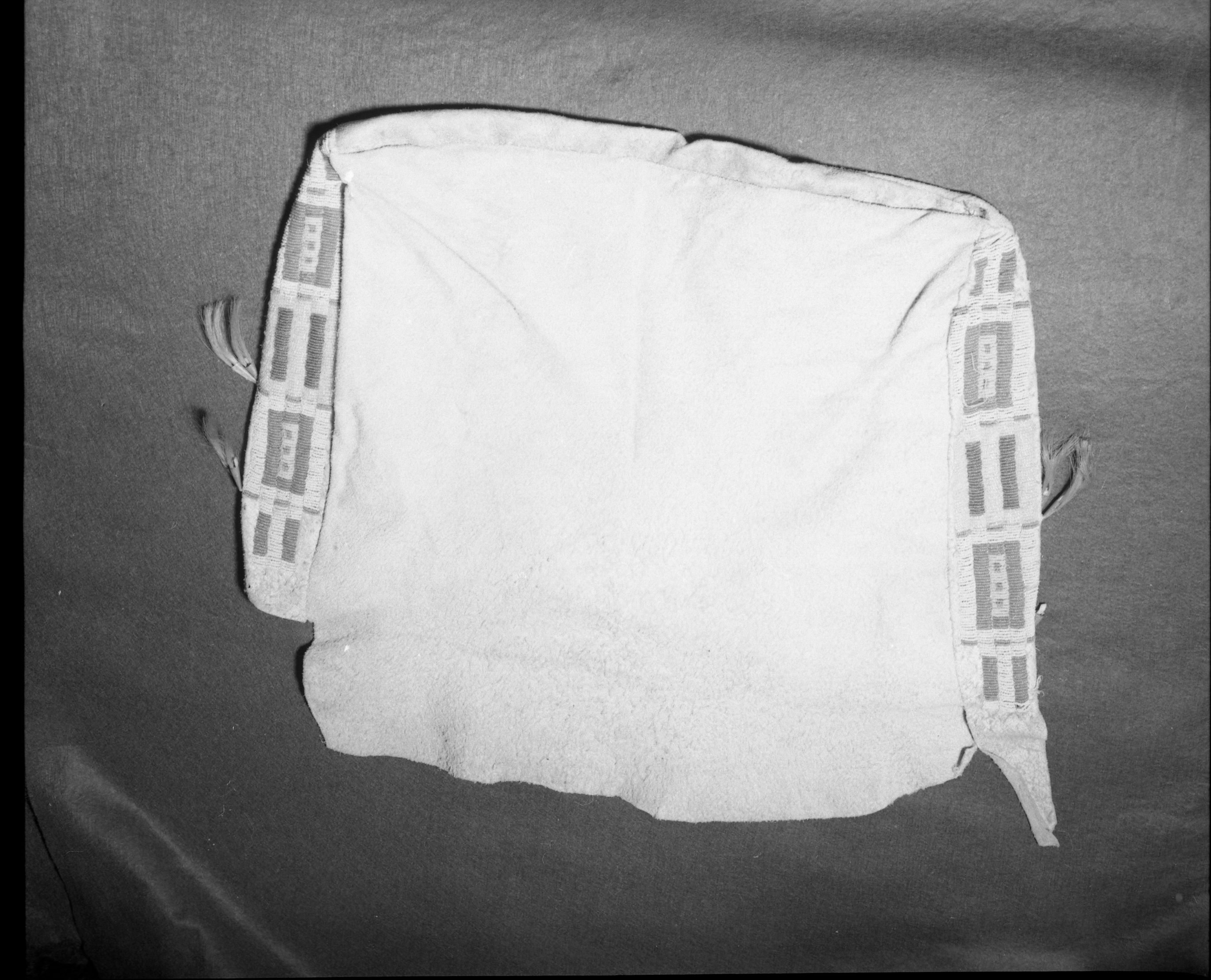 Mrs. Geraldine McConnell Collection. Object: Plains type beaded bag. Dimensions: Front - 22" x 13 1/2" Back - 18 1/2" x 18" wide at top and 16" wide at bottom. Side panels - 2 1/2" x 13 1/2" Bottom panel - 1 1/4" x 16 1/2". Technology & Materials: Brain tanned hide, sinew sewn with overcast stitch, turned right side out when completed. No welts used in seams. Beaded in lazy stitch in sinew using italian beads in opaque pink, dark blue, greasy yellow, turquoise, transparent clear, dark green, and medium blue. Three ties on body of sack with no matching holes on flap. In center top of front panel a 2" slit was made in the hide and sewn up with sinew, perhaps to take in excess hide. Brain tanned hide tabs project 5" from each side panel. Analine dyed horsehair emitting from tin cones completes decoration. Collection History: Purchased in a store in Mariposa, c. 1930's. Photographed by Michael Dixon January 1983. Catalogued by Craig Bates and Barbara Beroza. Yosemite collections, National Park Service.