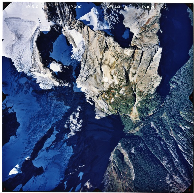Color aerial photograph of glaciated mountain peak with forested valleys below.