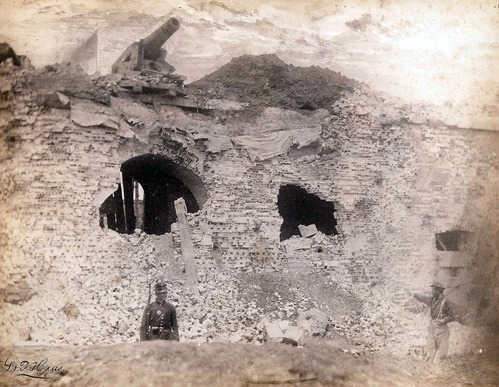 Black and white image of a wll of Fort Pulaski that has two large holes caused by the artillery bombardment. There is a union soldier in the foreground and a cannon hanging from the fort ledge at the top. 