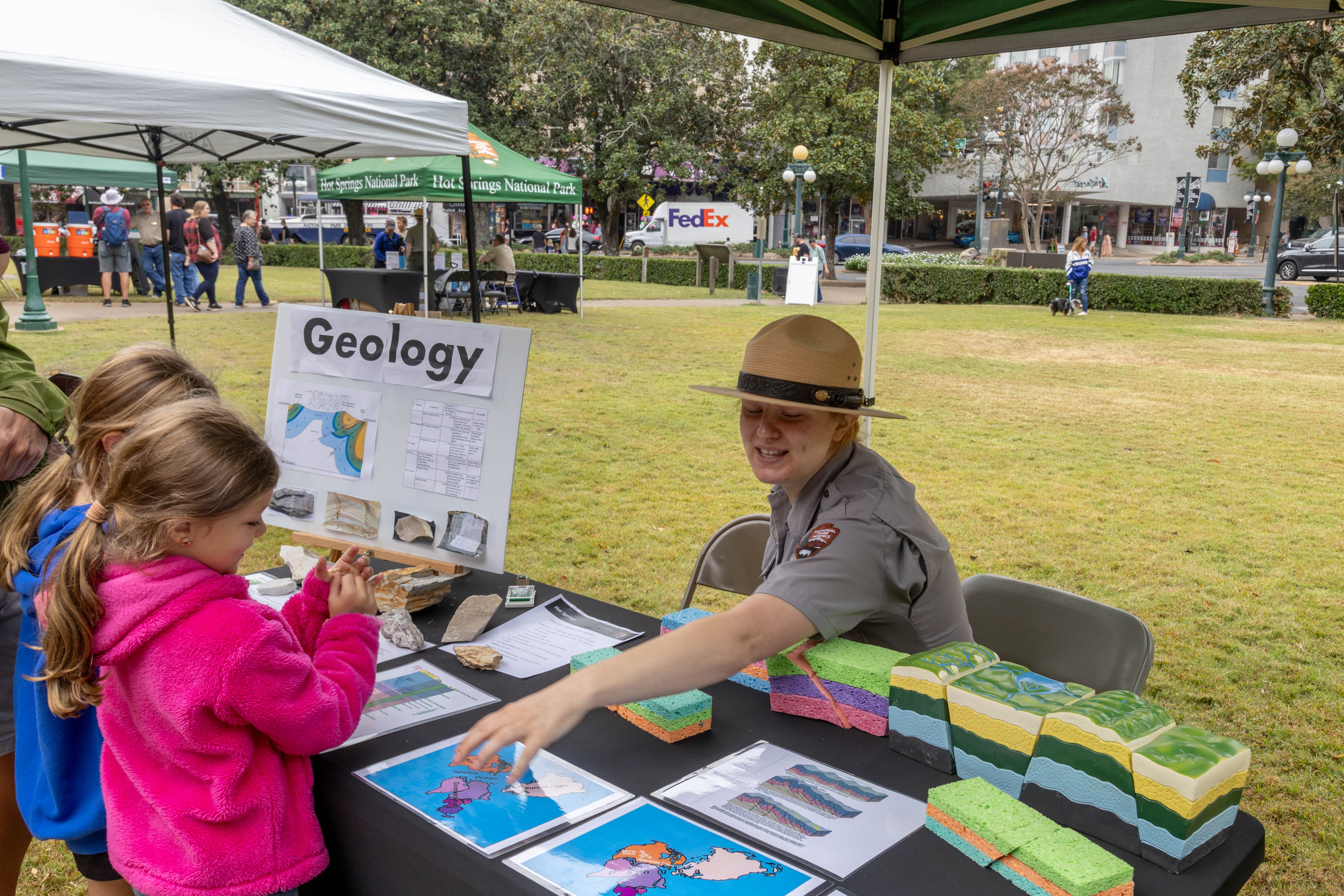 Park Ranger in grey shirt and beige hat interact with two young visitors at a table filled with interactive blocks