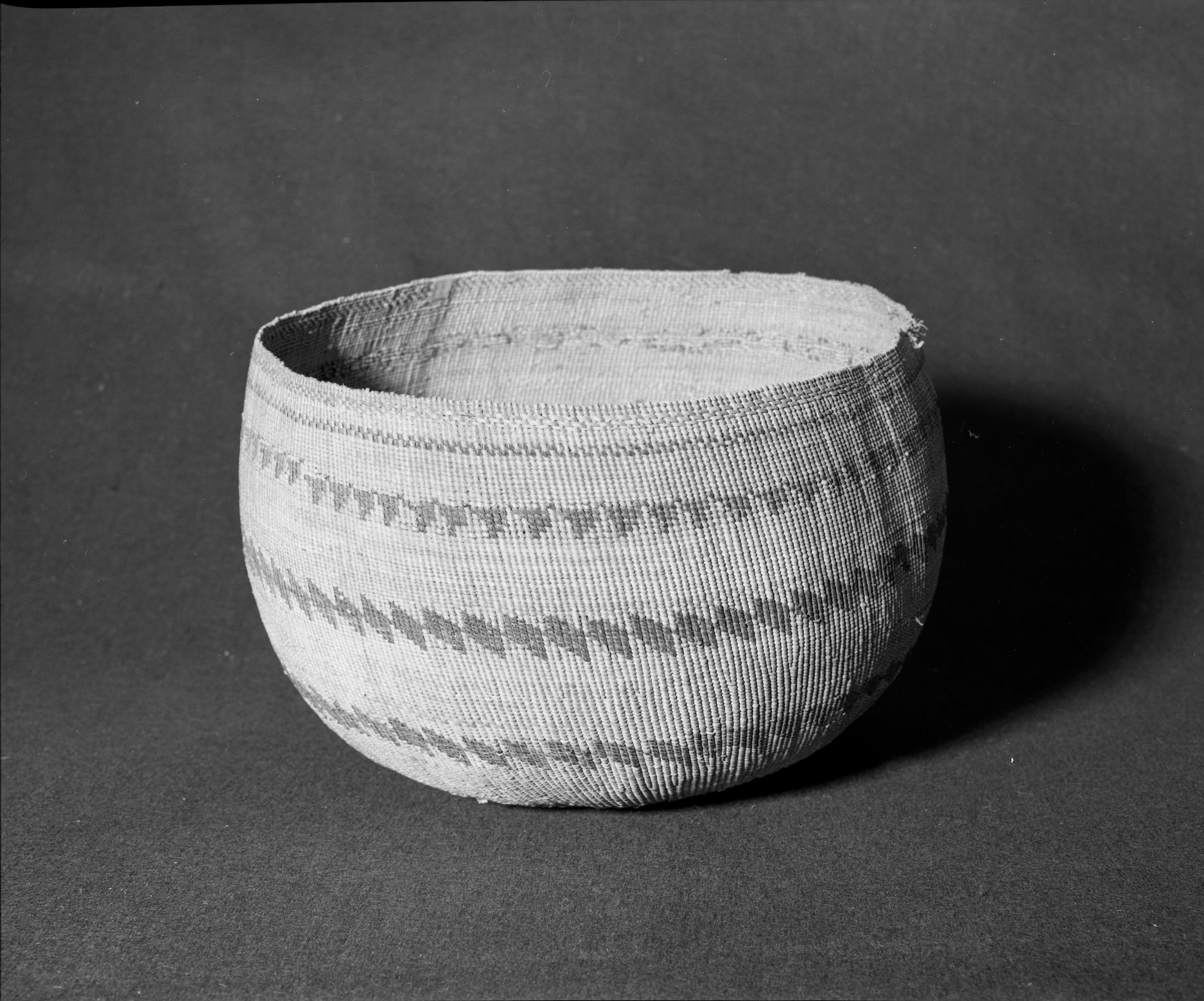 Marie Rozier Collection, Catalog No. 193. Object: Pomo twined basket. Dimensions: 14 x 10". Materials: willow sticks, sedgeroot, redbud. Technology: plain twined, down to right slant of turns, three rows diagonal twining near rim. Collection History: Unusual case of spiral lattice binding being used on a linear banded pattern Pomo basket. Reportedly given by the Miwok woman Sally to Mrs. Alice Wilson. Photographed by Michael Dixon, Dec. 1982. Catalogued by Craig Bates and Barbara Beroza. Yosemite Collections, National Park Service.