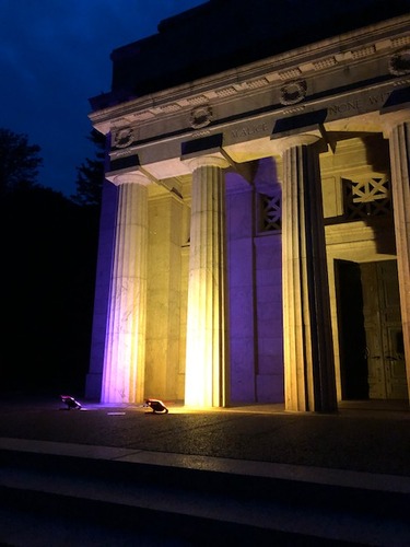 Columns of a memorial lit purple and gold at night