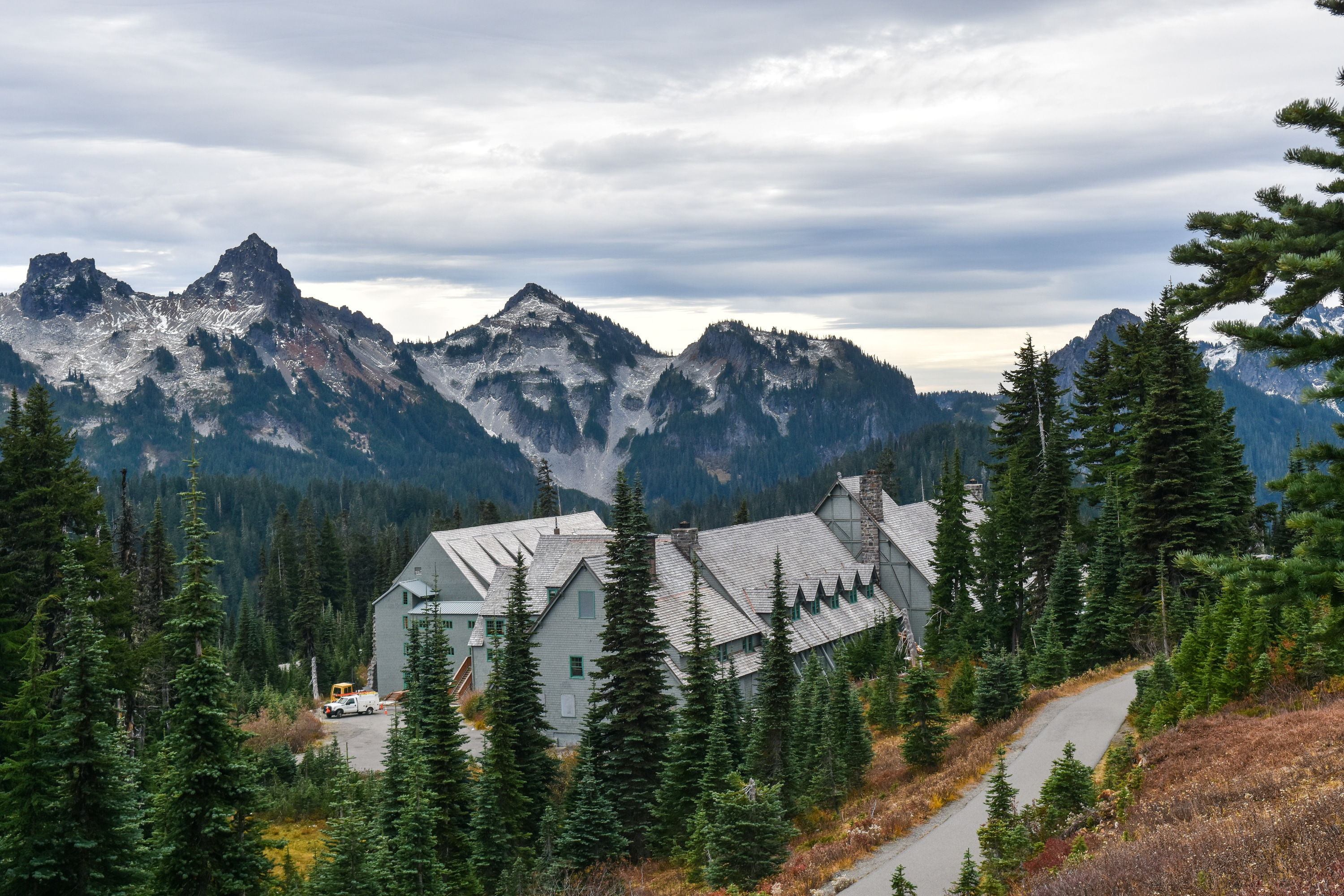 A building sits between the trees with mountains looming in the background.