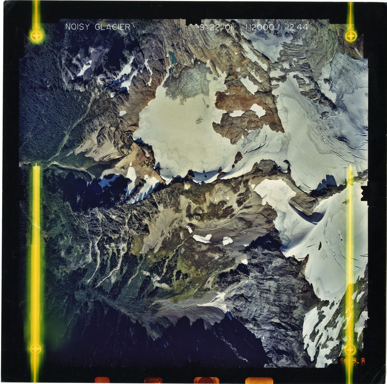Color aerial photograph of glacier on mountain peak, surrounded by forested valleys.