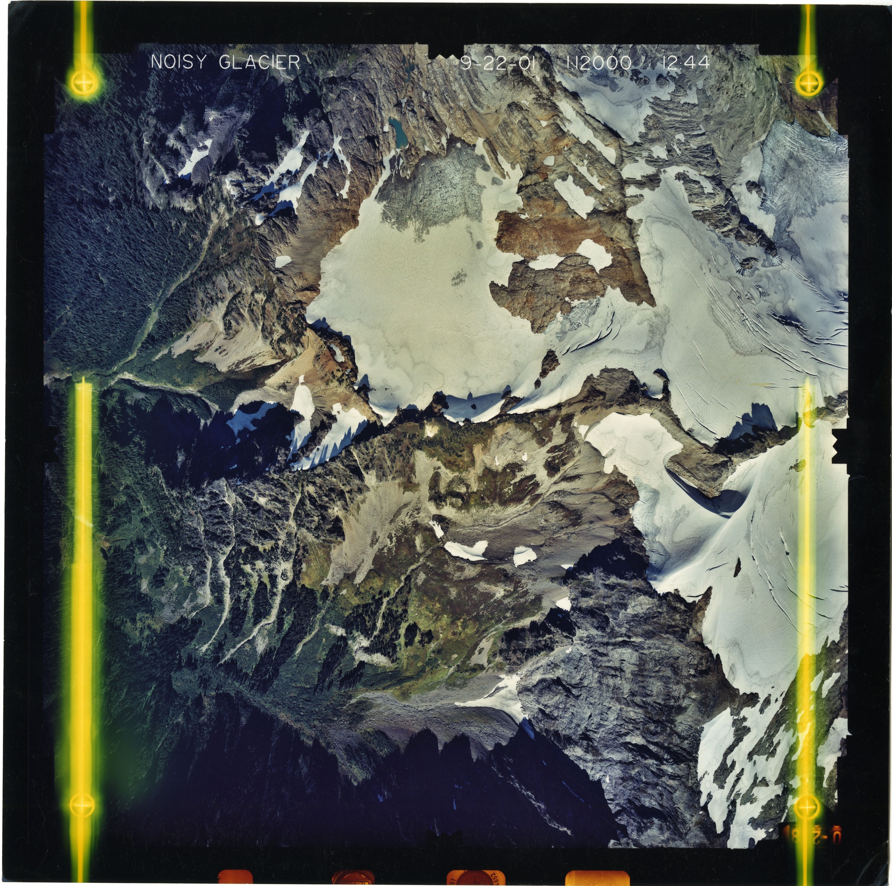 Color aerial photograph of glacier on mountain peak, surrounded by forested valleys.