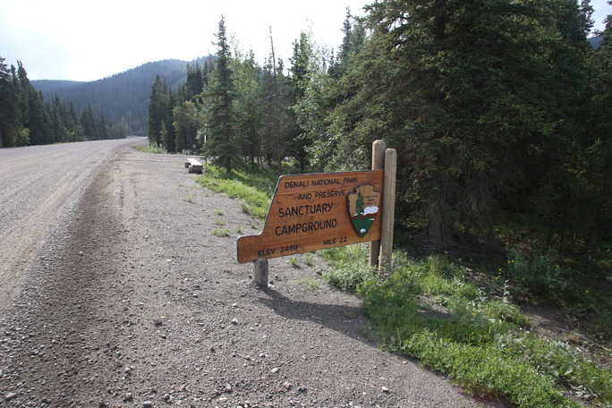 A wooden sign on the side of a gravel road which reads "sanctuary campground elevation 2,400 feet mile 22"