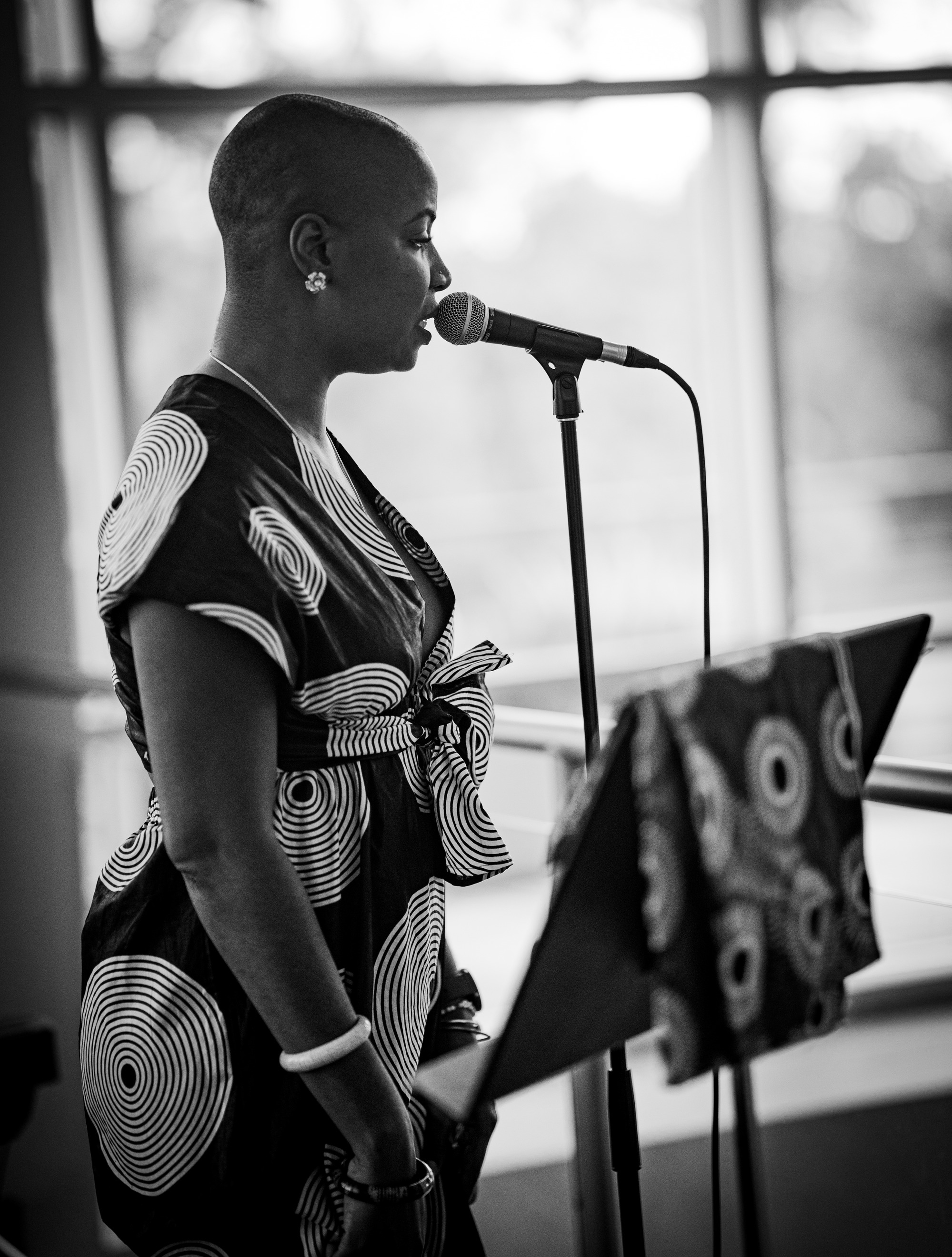 Black and White picture. Afro-Cuban woman singing into mic, standing beside music stand