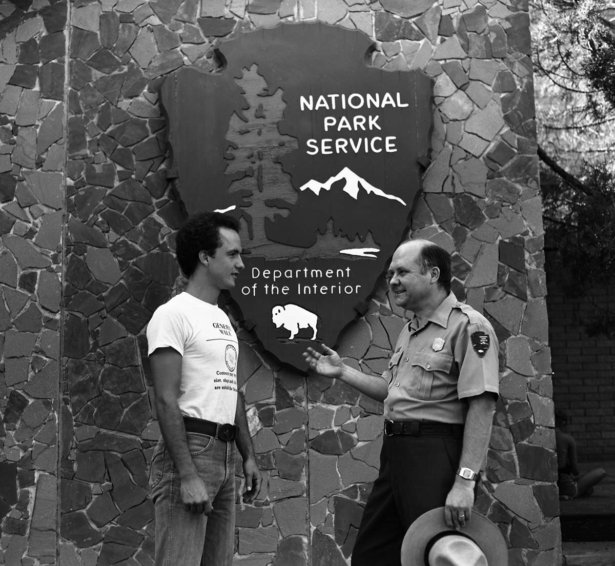 Victor L. Jackson, Chief Park Naturalist and 1982 Freeman Tilden Award winner for outstanding interpreter of the year, speaking with man in front of the Mission 66 Visitor Center and Museum arrowhead.