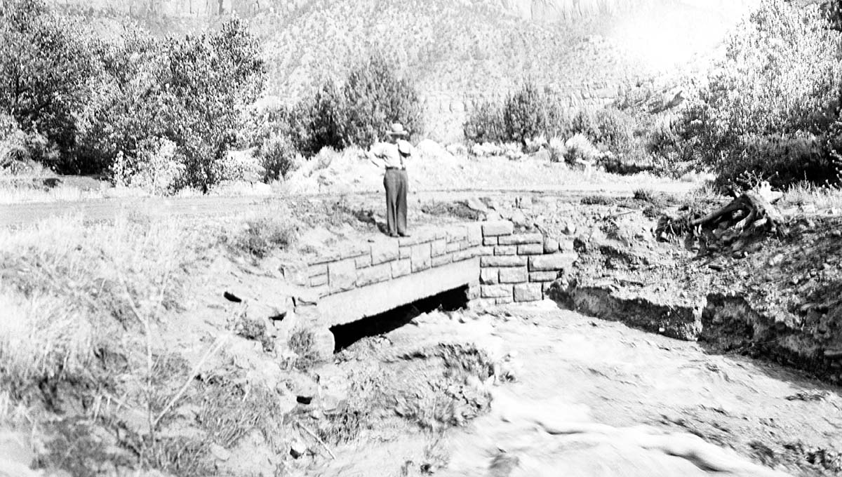 Ranger observing Oak Creek flood filling the channel under the bridge near the utility area. Notable erosion of the banks.