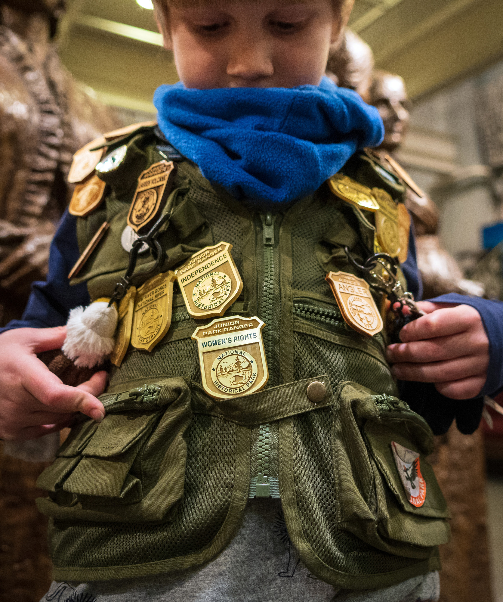 A boy wearing a green vest covered in gold plastic badges shows off his Women's Rights badge.