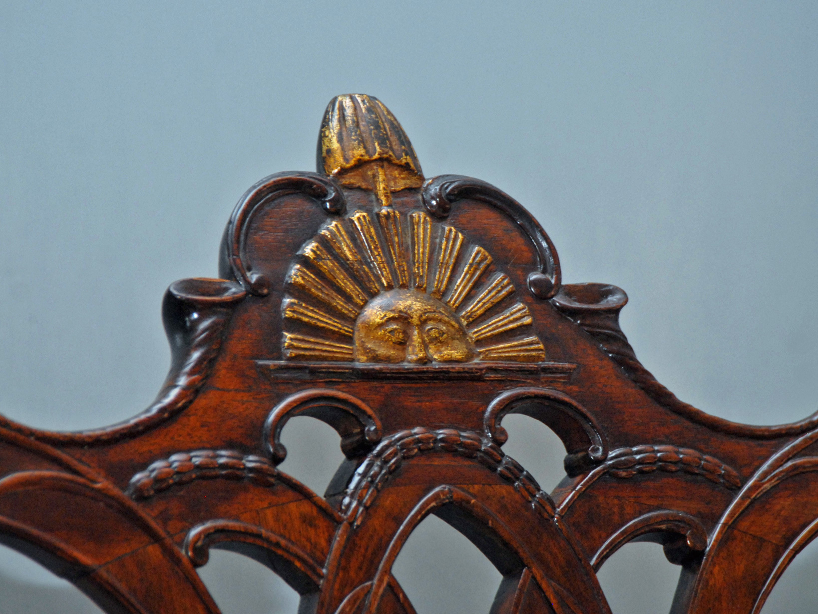 Detail showing a golden half-sun carved into the top back of a wooden chair.  A liberty bell and liberty cap rise from the top of the sun.