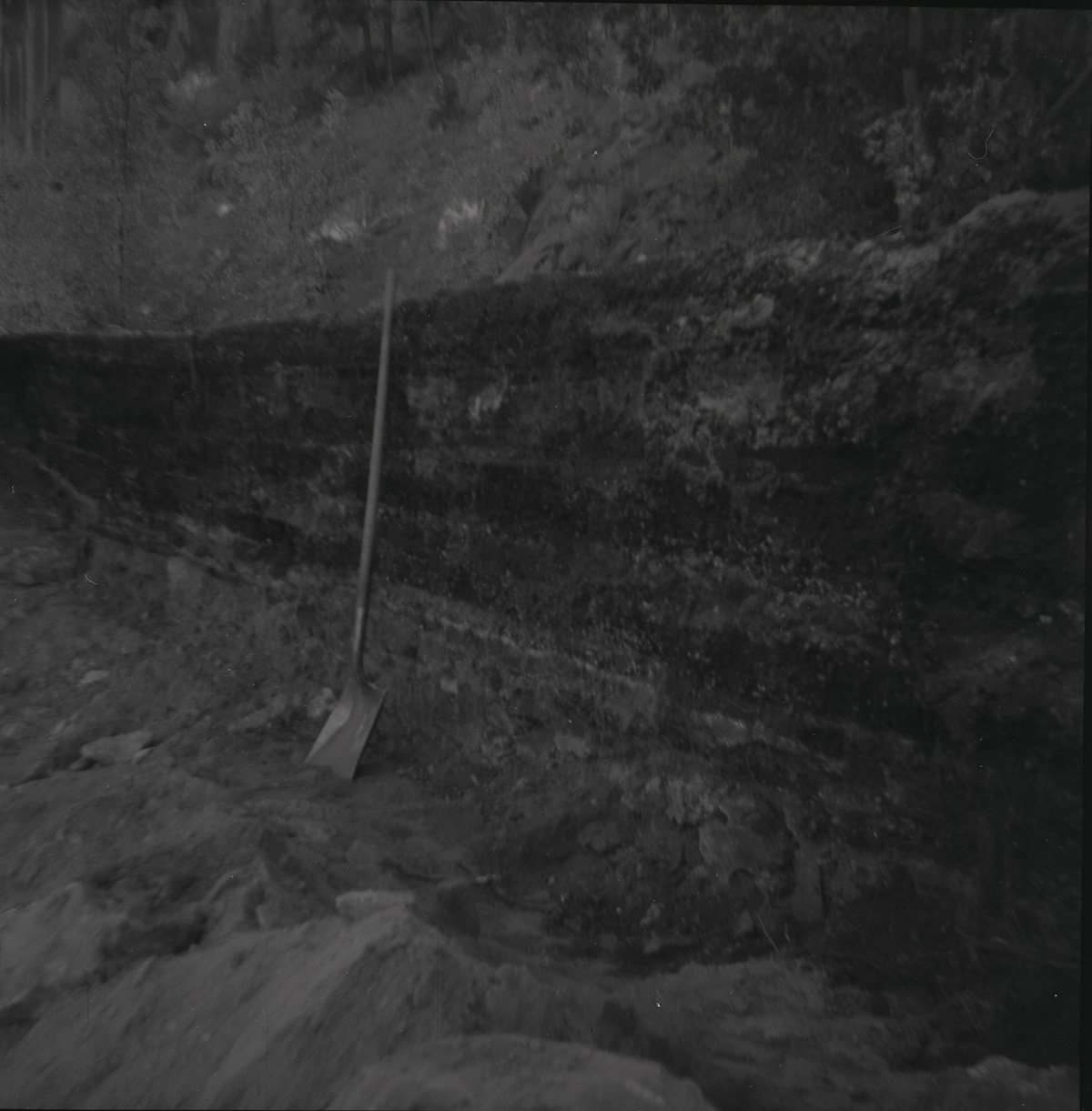 Shovel leaning against rock retaining wall alongside road at the tunnel during rebuilding.
