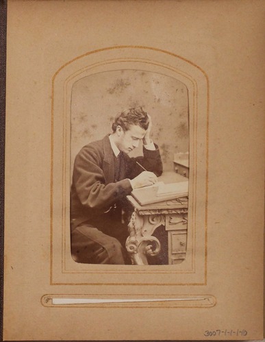 Black and white photograph of young man writing at desk.