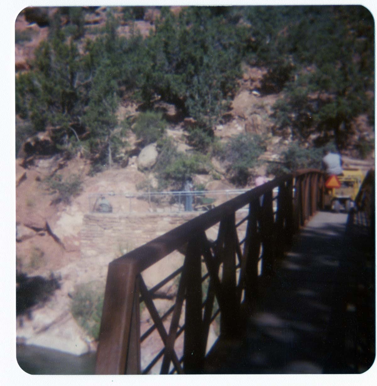 Man driving sweeper equipment across the new Grotto footbridge after its placement on stone abutments. Men working on trail in background.