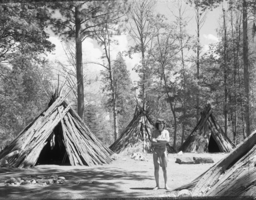 Re-constructed Indian Village behind Visitor Center. 1979 or 1980. Fermin Salas, Indian Cultural Demonstrator in foreground.