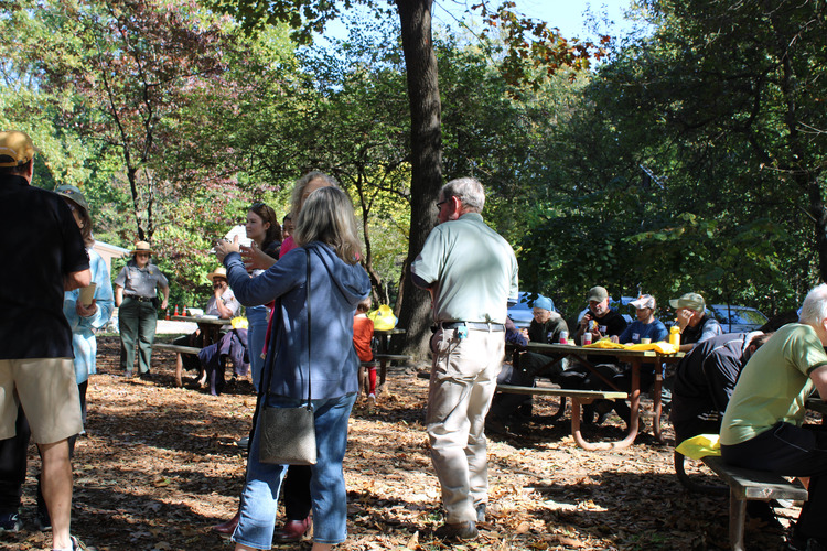 Volunteers chatting, seated at picnic tables, eating snacks, and waiting for the volunteer recognition event to begin. 