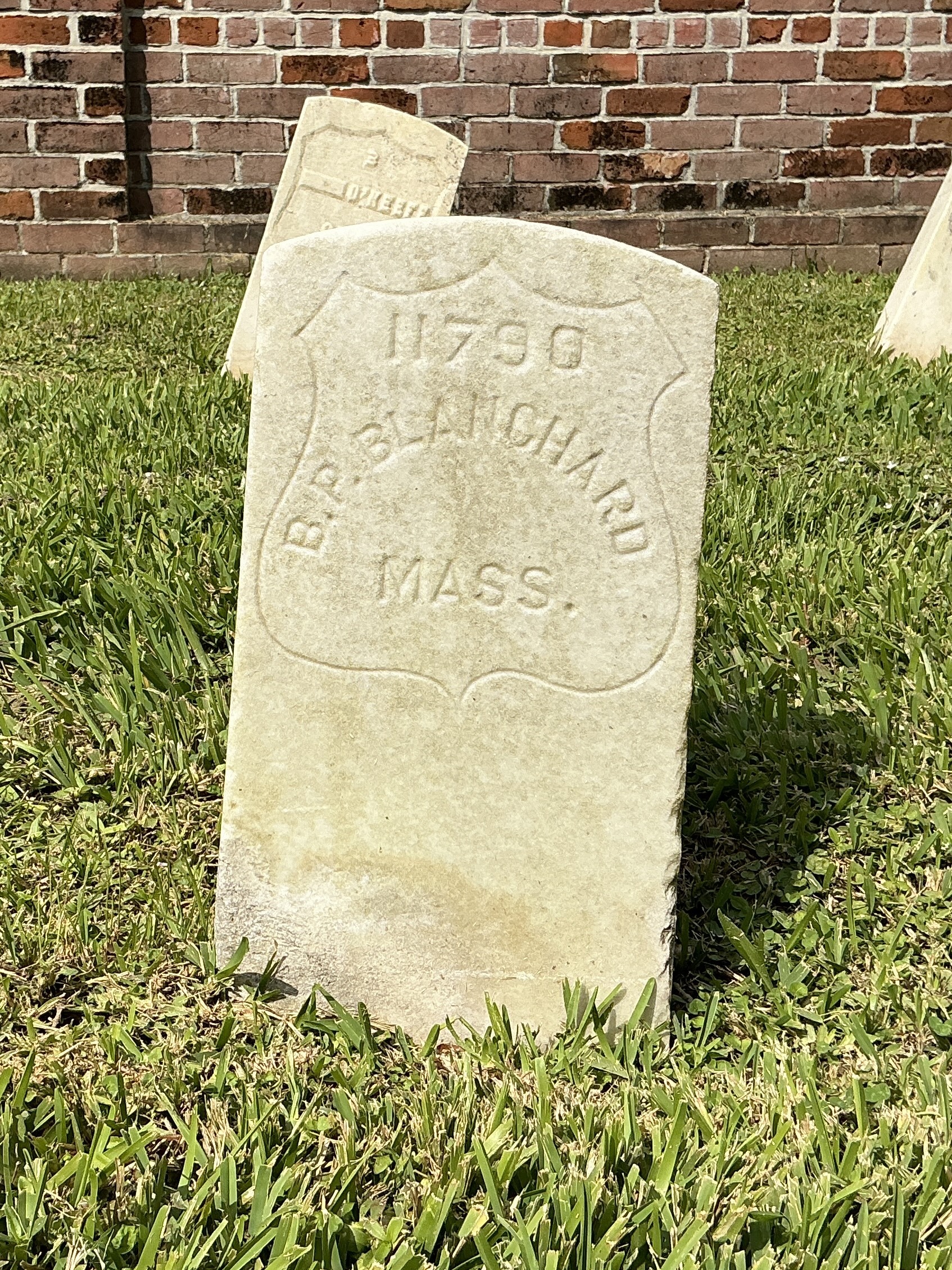 Front of historic upright marble headstone with incised shield face.