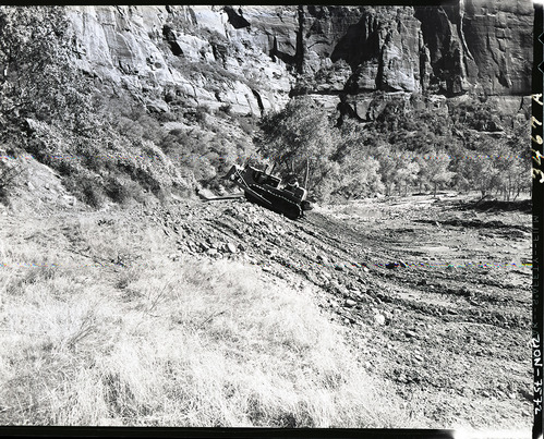 Road repair of flood damage on valley road by packing road slope with bulldozer.