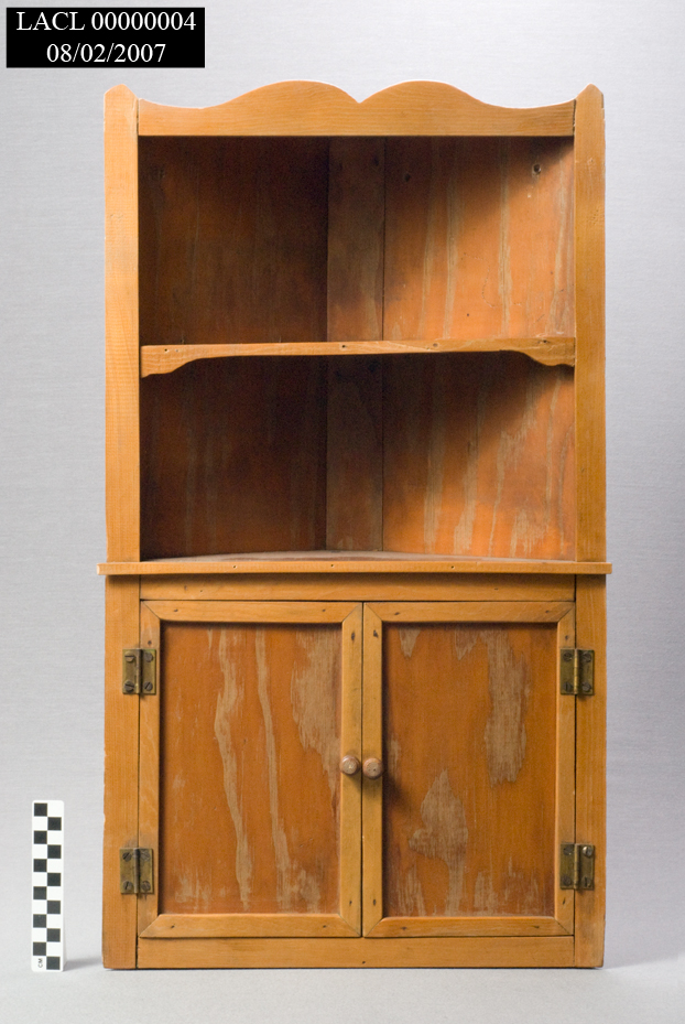 Triangular, light brown wooden shelf. Top edge is scalloped, and the front has two shelves at the top. 