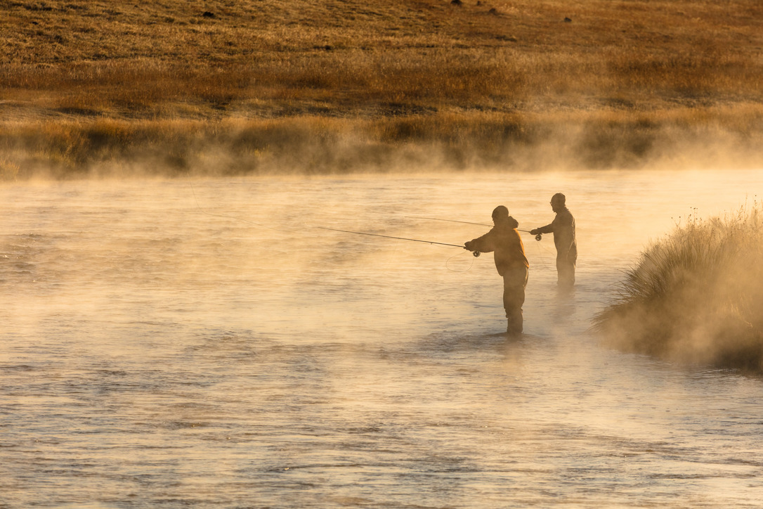 Two men standing in the water fishing on a cold, misty morning.