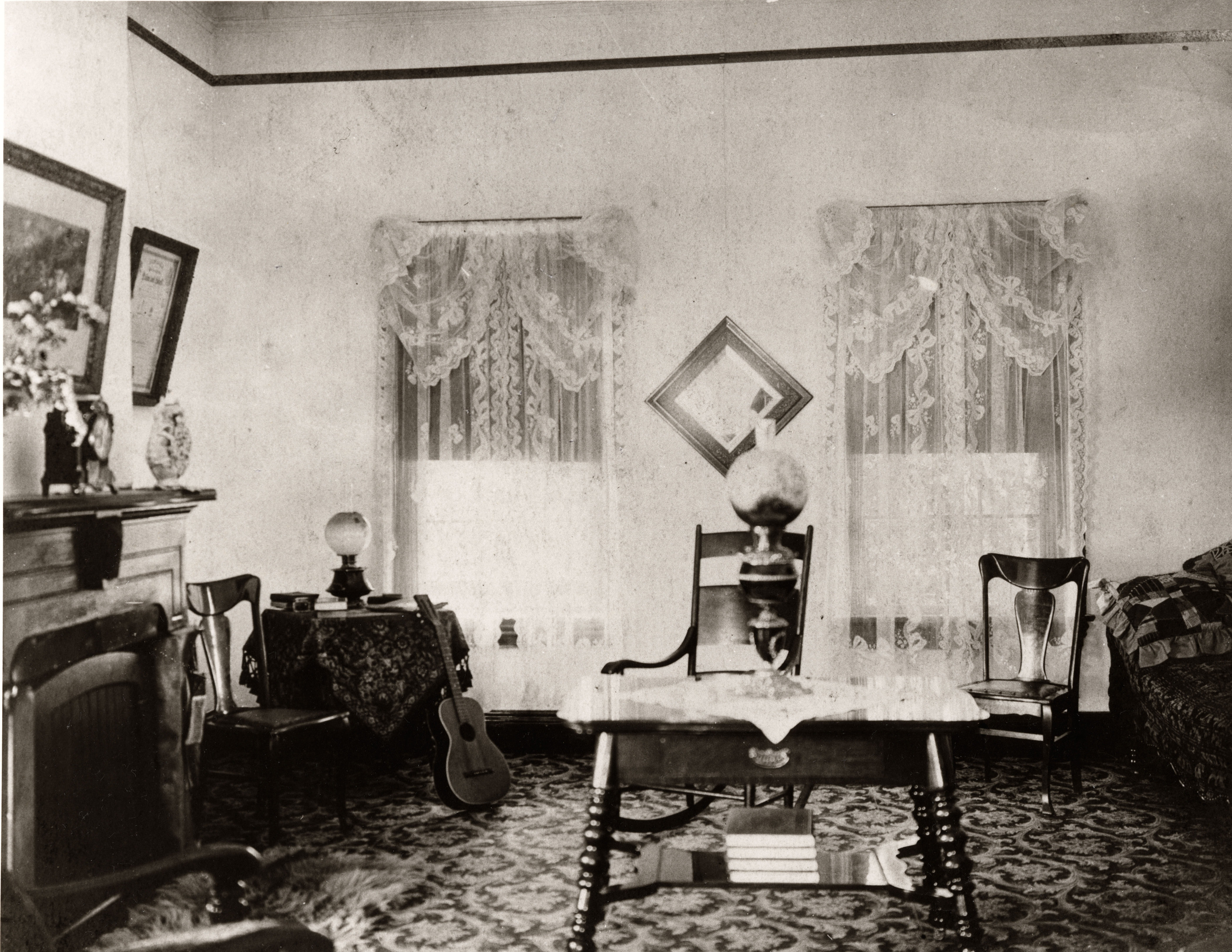 Black and white photograph of a sitting room with chairs, table, and fireplace
