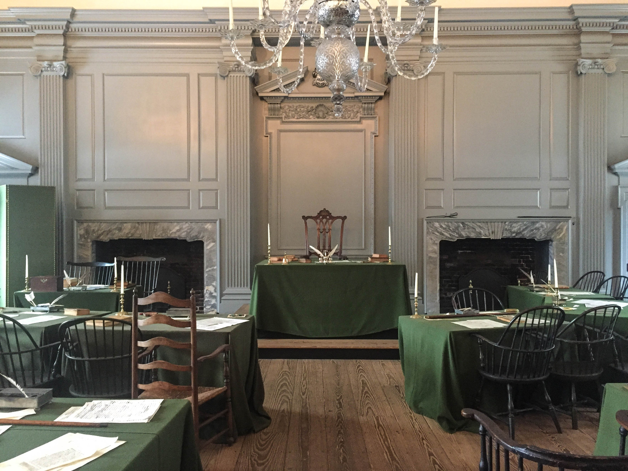 Meeting room with lines of tables and chairs covered with green table cloths, candles, books, papers, and quill pens