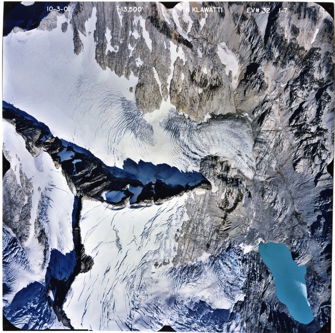 Color aerial photograph of glacier, snowfields, and alpine lake on mountain peak.