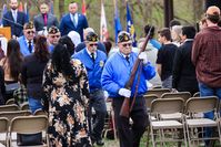 Speakers and audience members stand facing the flag as uniformed American Legion members exit in single file. The Legionnaires in front and back of the color guard carry rifles.