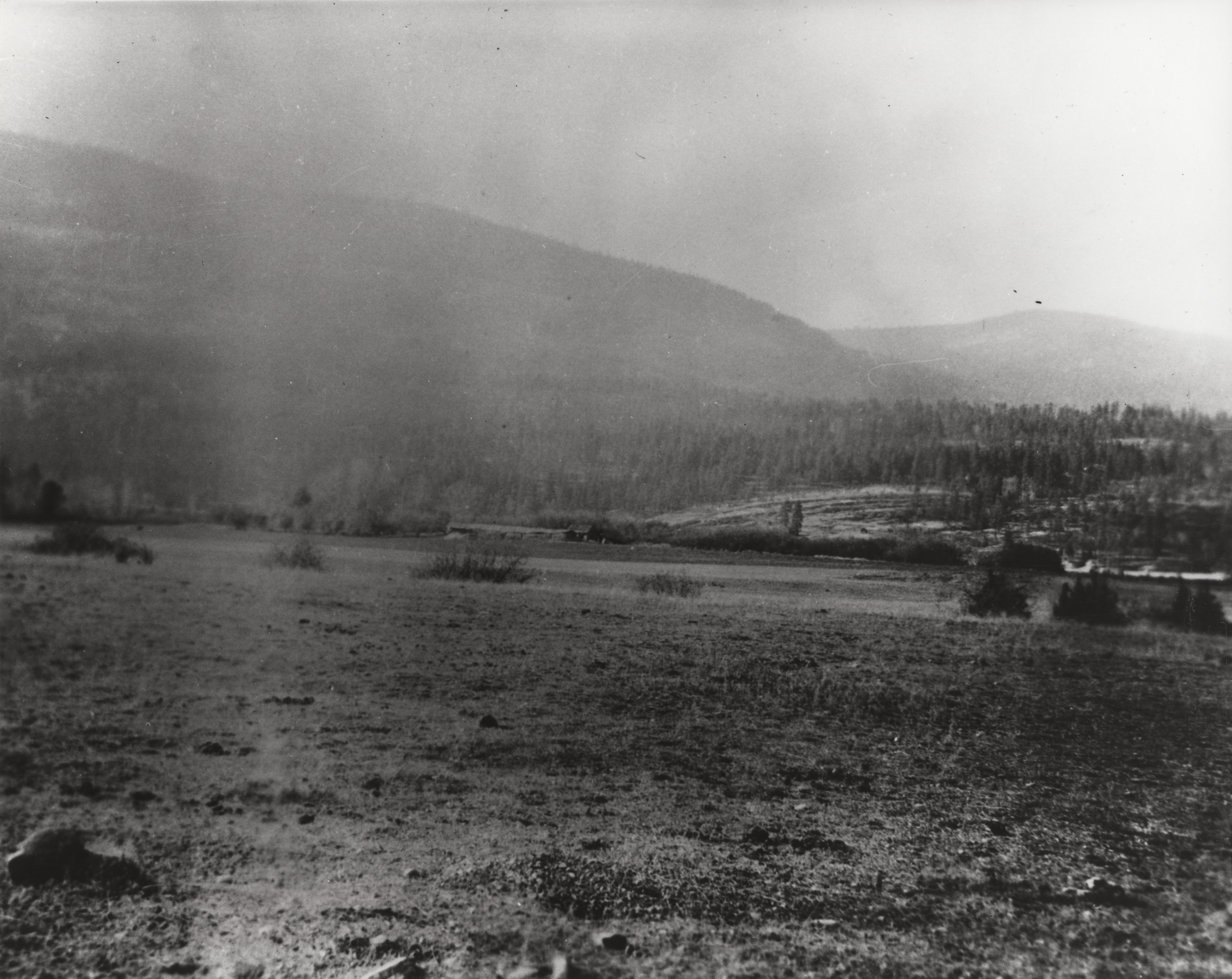 Faded black and white photograph of a bare field with rolling hill in the background
