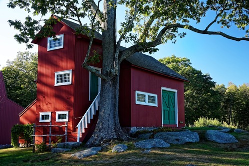 A red building with two green doors, white trim around its many windows and a tree near the front door.