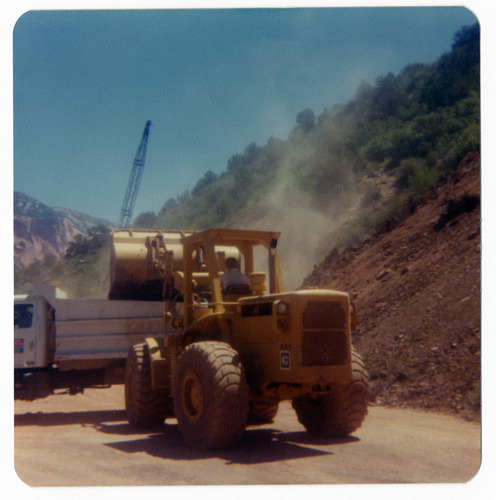 Excavator clearing dirt and rocks into dump truck to repair road in Kolob Canyon.